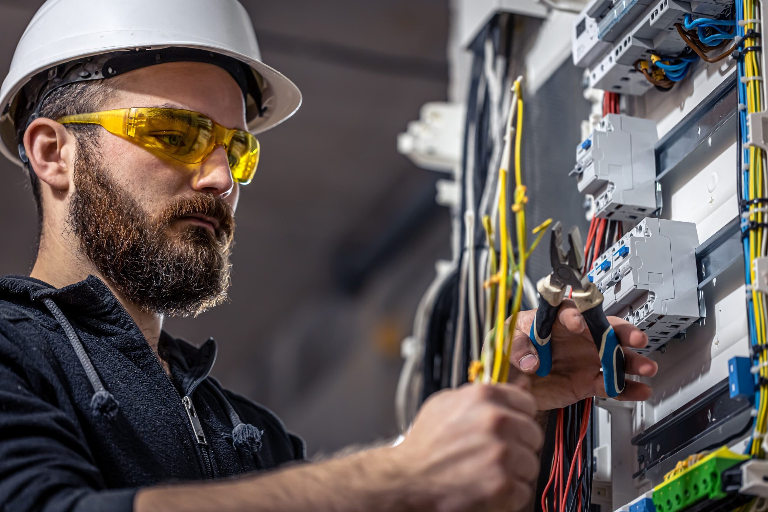 a male electrician works in a switchboard with a wrench