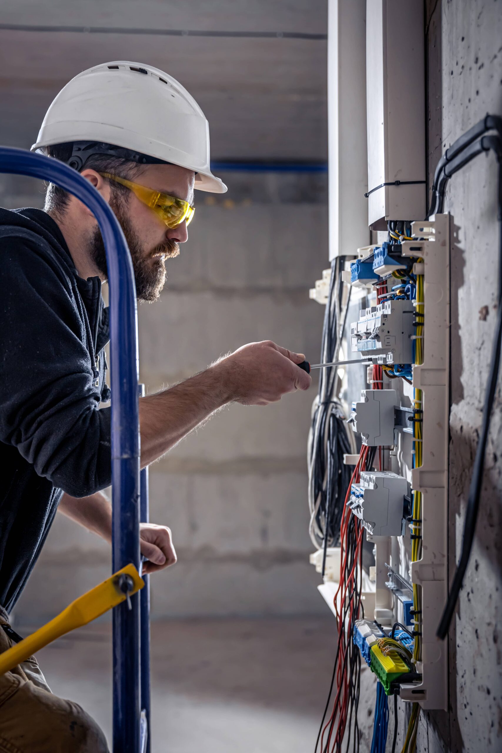 a male electrician works in a switchboard with a screwdriver