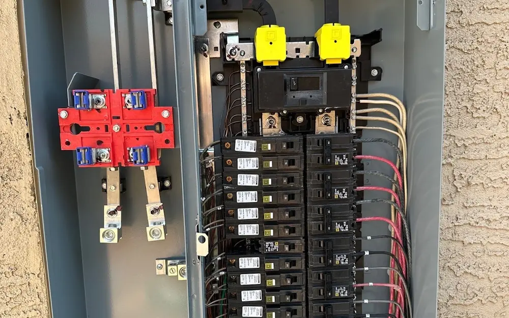 Open residential electrical panel with breakers and wiring, mounted on a stucco wall at a Phoenix-area home