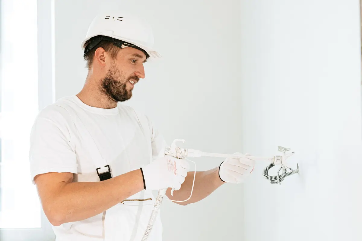 Electrician in a white hard hat and work gloves wiring a fixture on a wall during a home electrical job