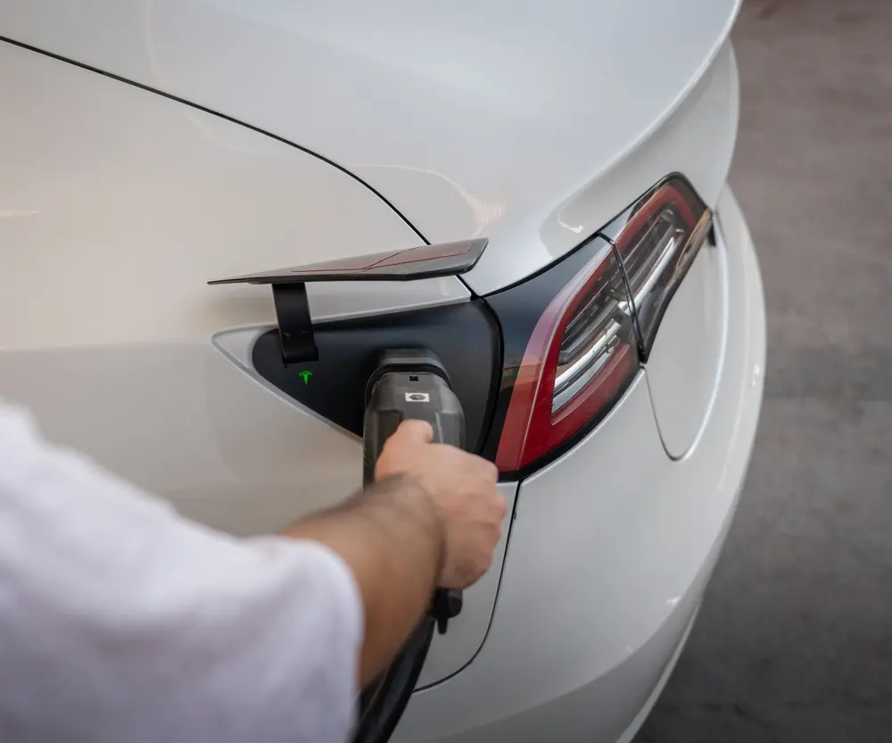 Hand plugging a home charger cable into an electric car, the kind of new load a Phoenix-area panel must support