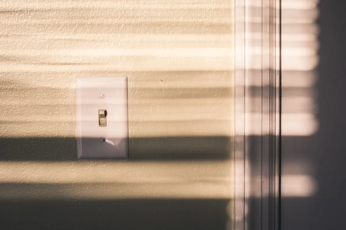 Light switch on a wall with shadows from window blinds