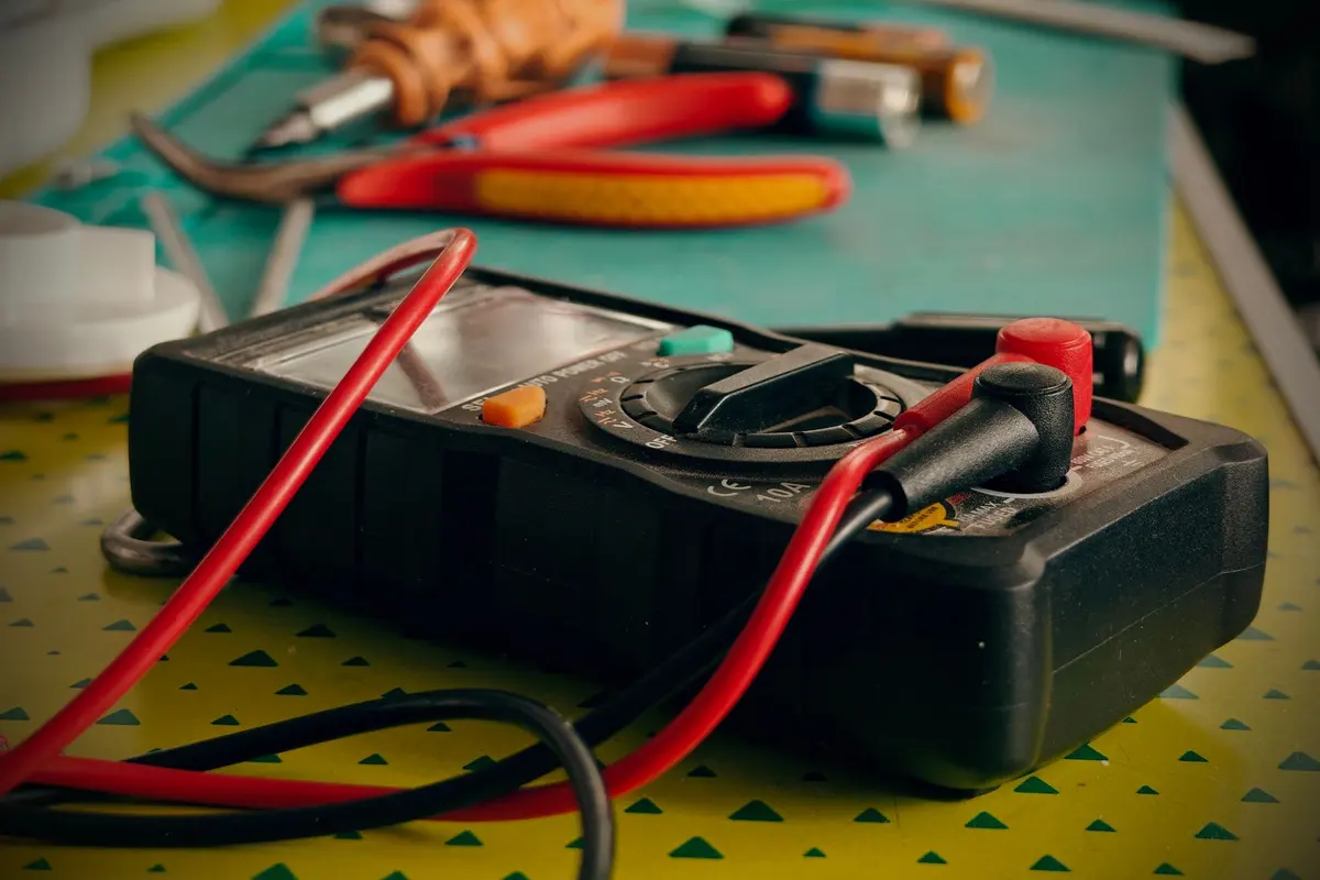 Multimeter, pliers and screwdriver laid out on a green work mat