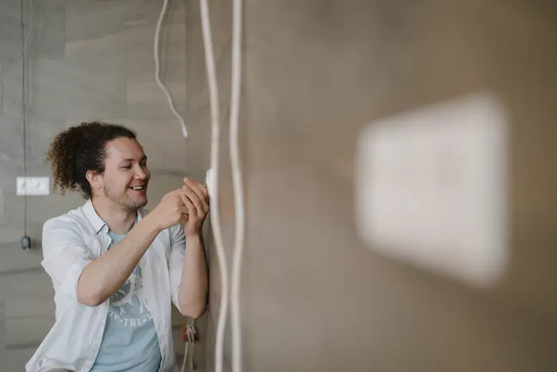 Man adjusting an outlet on a wall with wires hanging beside it